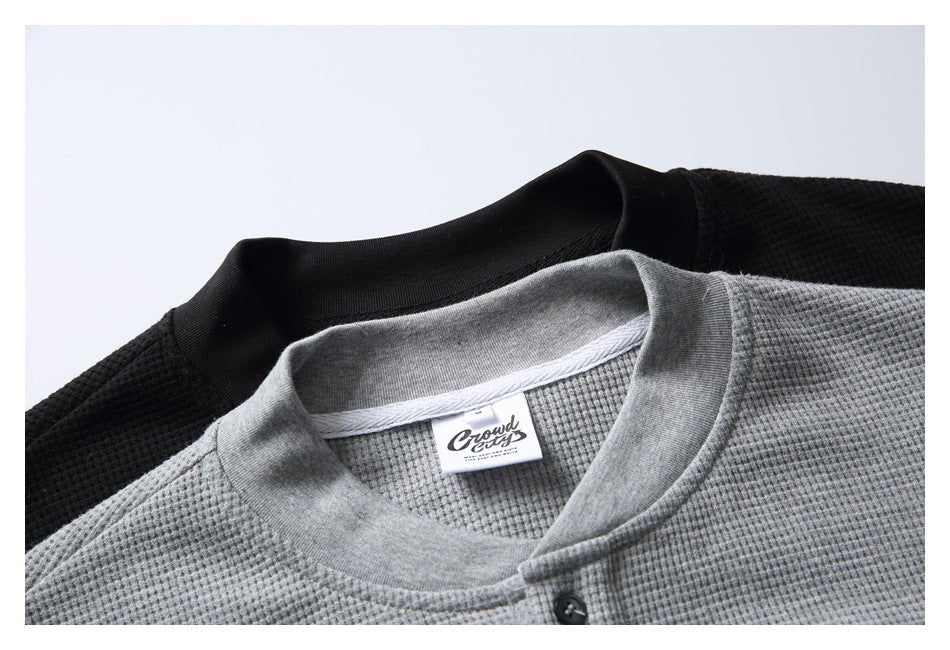 Close-up of overlapping black and gray textured shirts, showing their ribbed crew necklines and a small neck label.