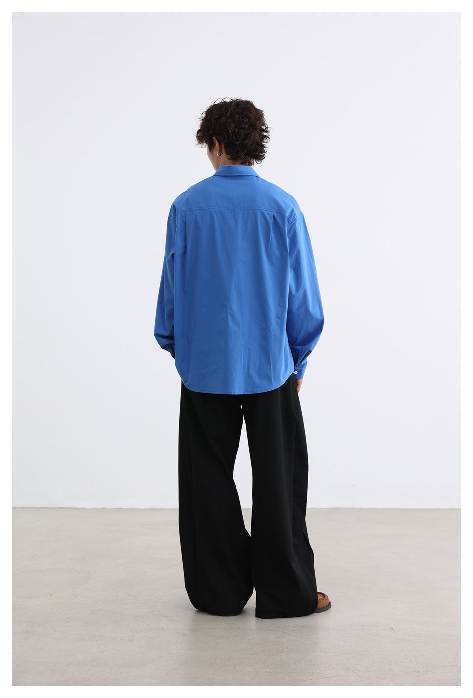 Back view of a model wearing a blue oversized shirt with wide-leg black pants