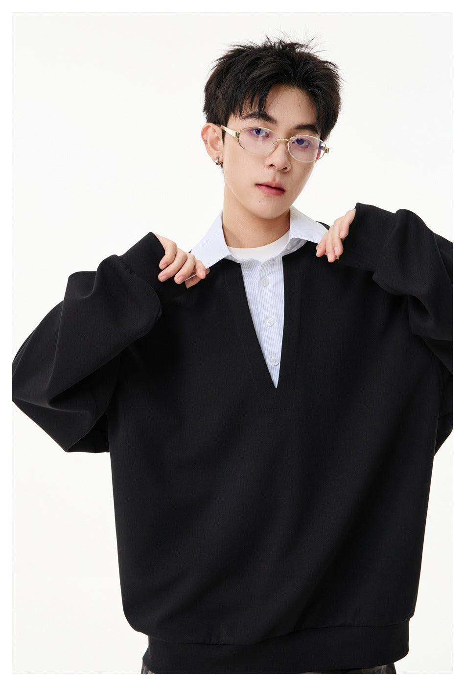 Close view of a model wearing a black oversized V-neck pullover over a white collared shirt.