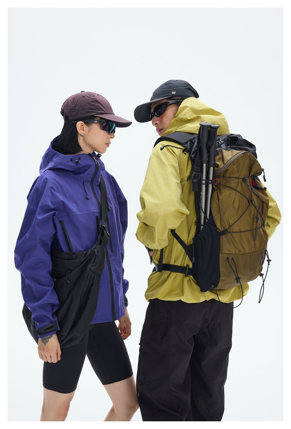 Close view of two hikers in purple and yellow hooded jackets, with a large brown backpack and black gear straps.