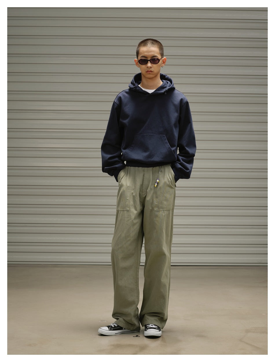 Front view of a model wearing a dark navy pullover hoodie with a kangaroo pocket and loose olive trousers.