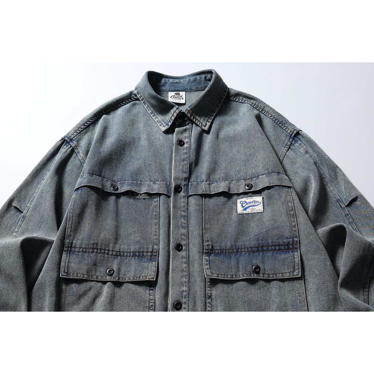 Front close-up of a faded blue-gray denim shirt jacket with a pointed collar, black buttons, and two large flap pockets.