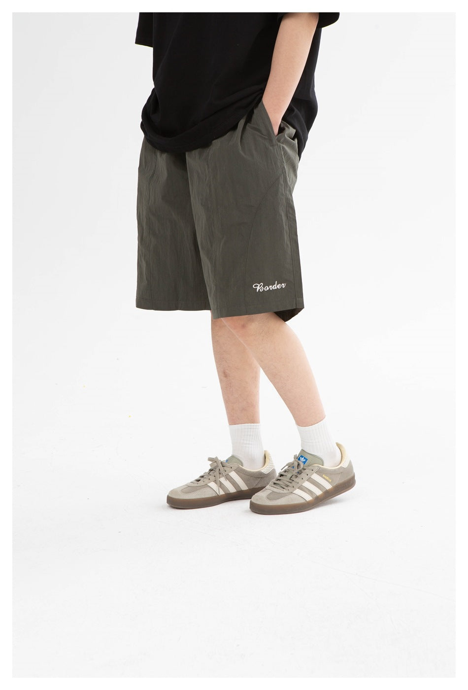 Cropped side view of a model wearing dark olive knee-length shorts with white script near the hem.