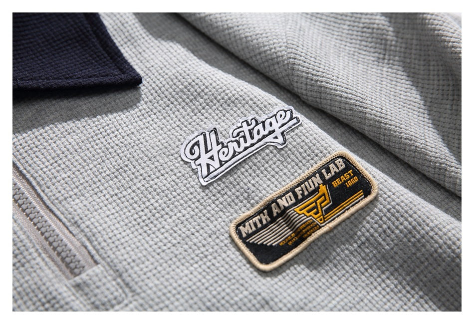 Close-up of two embroidered patches on the light gray textured pullover.