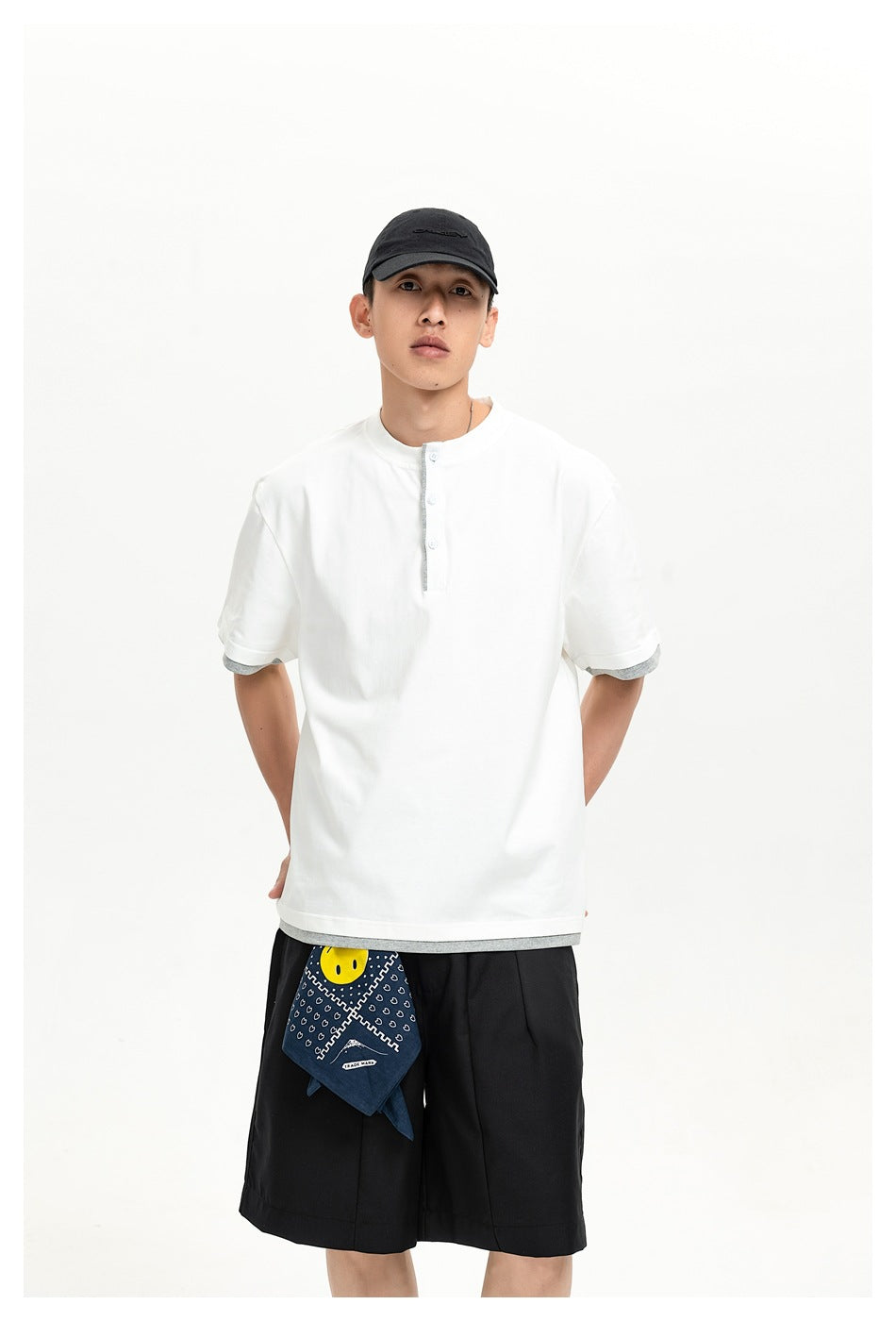 Model wearing a white short-sleeve Henley shirt with gray trim, black shorts, and a patterned bandana.