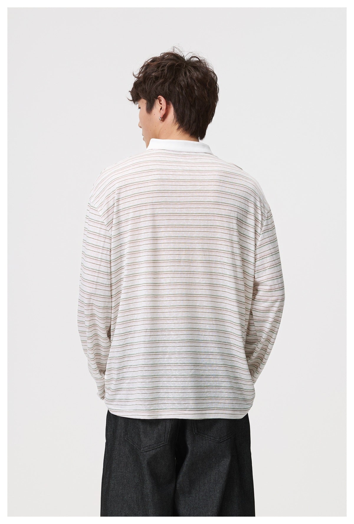 Back view of a model wearing a loose white top with fine muted horizontal stripes and long sleeves.