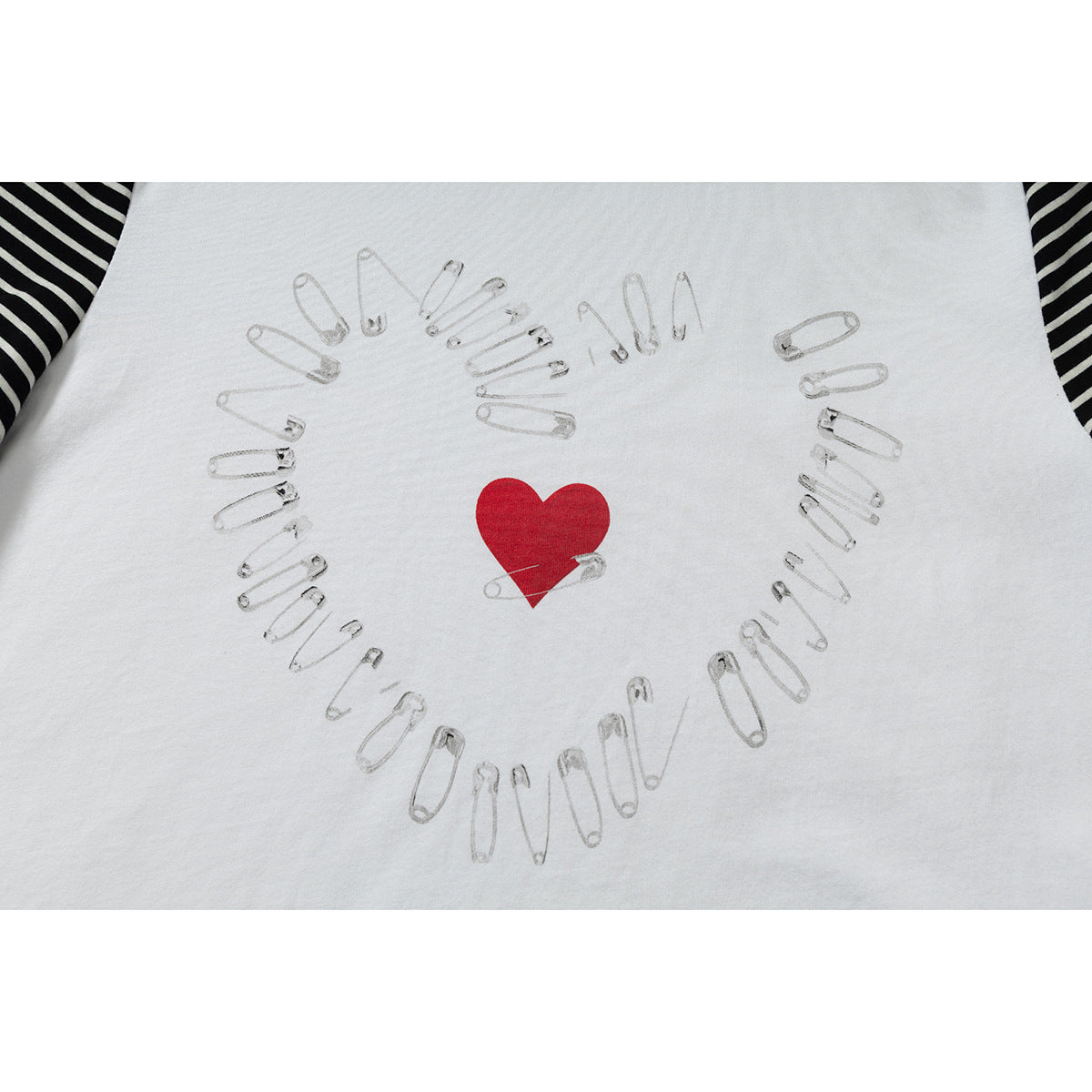 Close-up of a white T-shirt graphic: a red heart surrounded by safety-pin illustrations, with striped sleeves at the edges.
