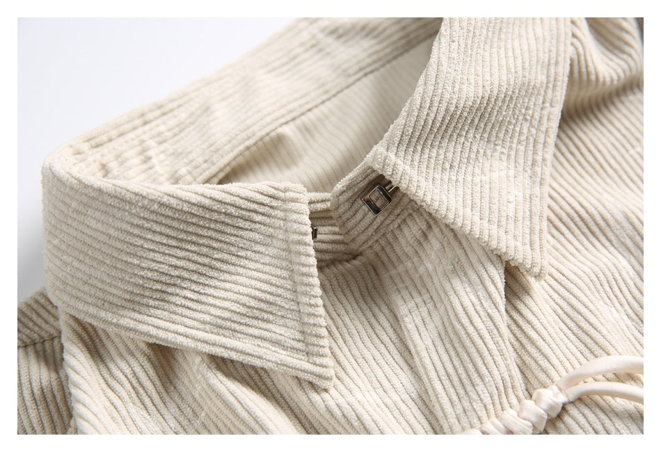 Close-up of a cream ribbed corduroy garment showing its wide collar and small metal clasp.