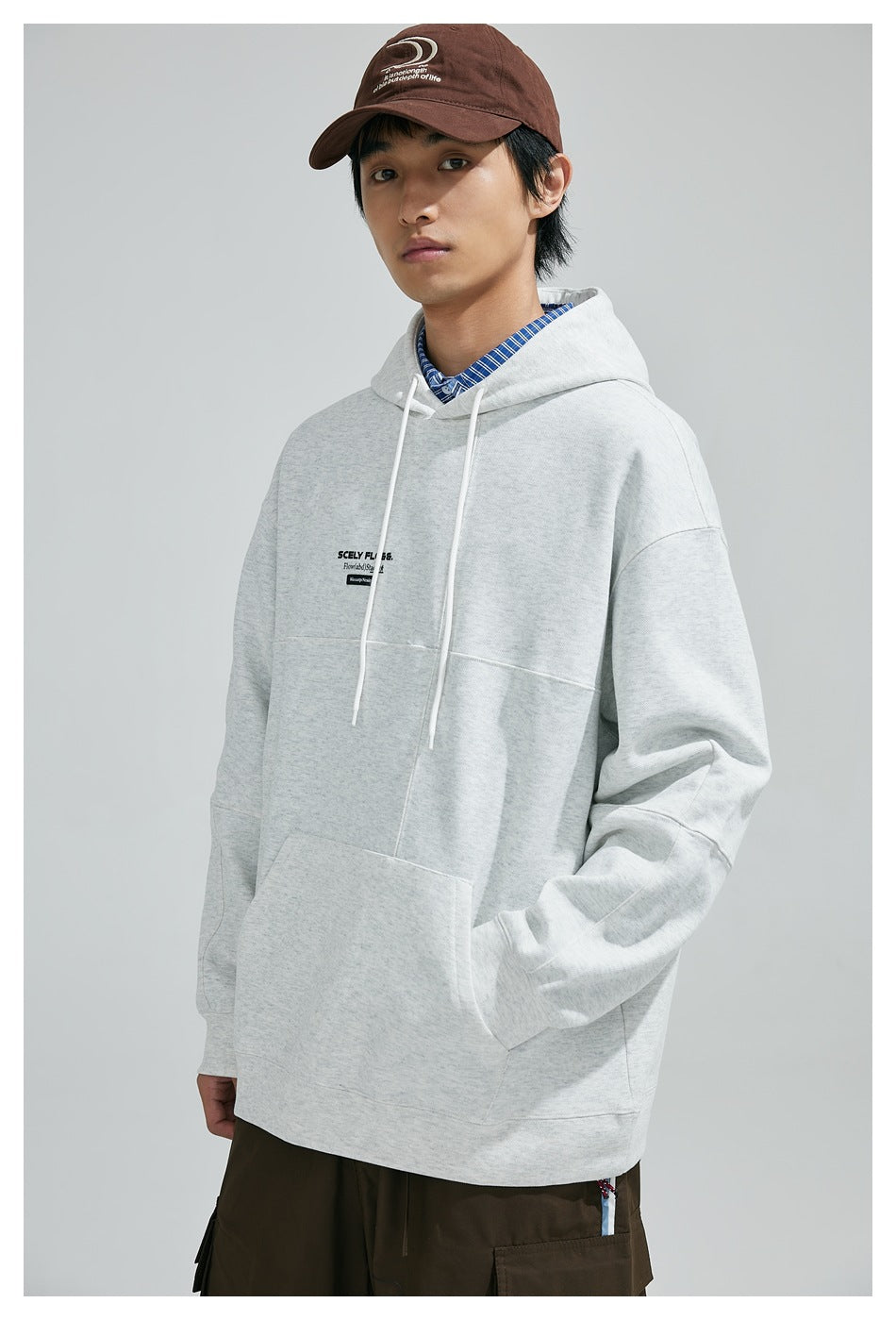 Model wearing a light gray hooded sweatshirt with white drawstrings, a kangaroo pocket, and small chest text.