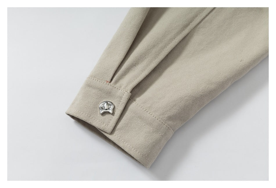 Close-up of a beige garment cuff with stitching and a small silver decorative button.