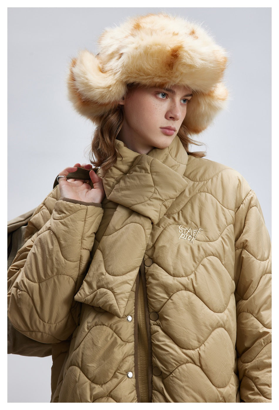 Close-up of a model in the khaki quilted jacket showing the wavy quilting, snap buttons and scarf piece