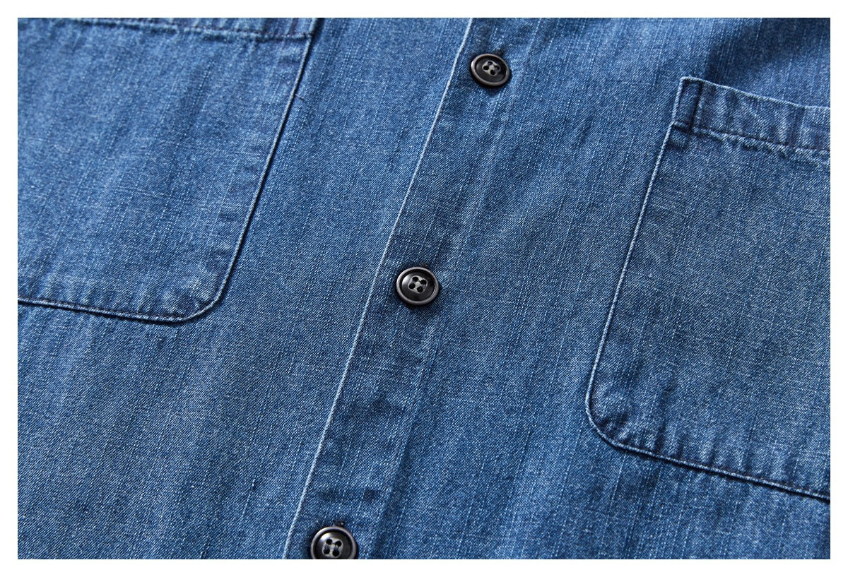 Close-up of a blue denim shirt front with black buttons and two patch pockets.