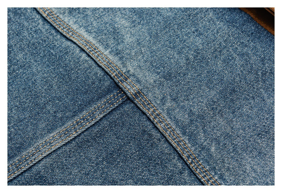 Close-up of faded blue denim panels and diagonal seams with tan topstitching.