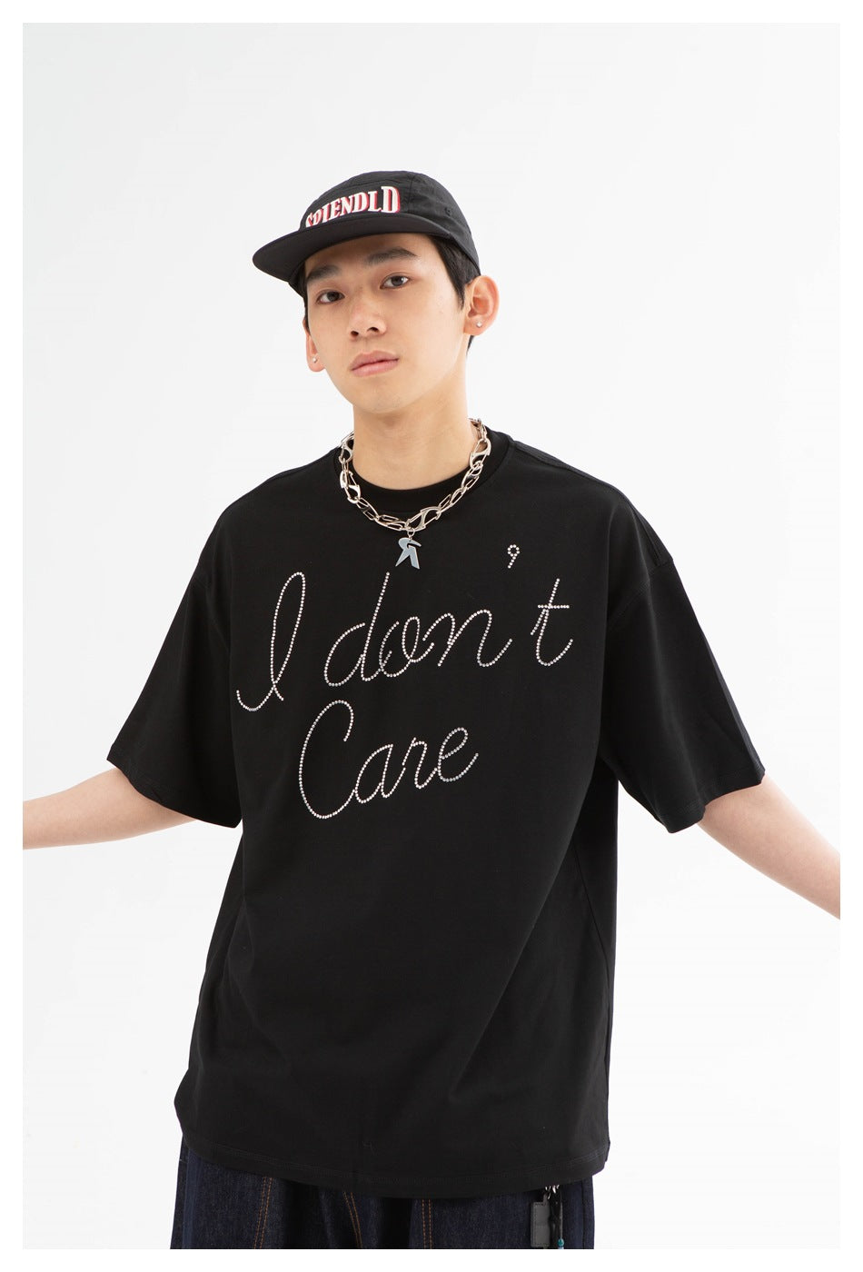 Model wearing an oversized black T-shirt with rhinestone “I don't care” script and a black cap.