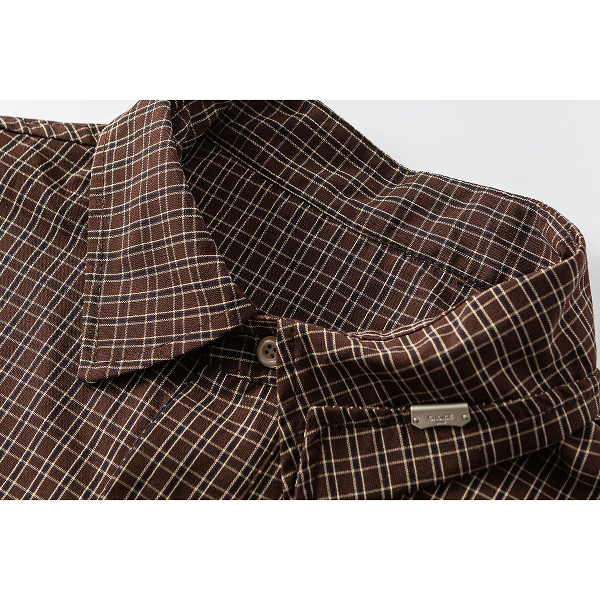 Close-up of a brown plaid shirt collar with a button and small metal emblem.