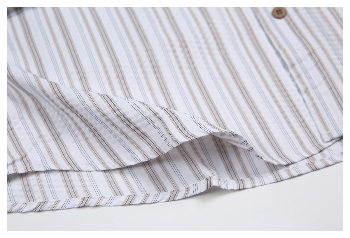 Close-up of a white button-up shirt with fine gray and beige stripes, showing the curved hem and a brown button.