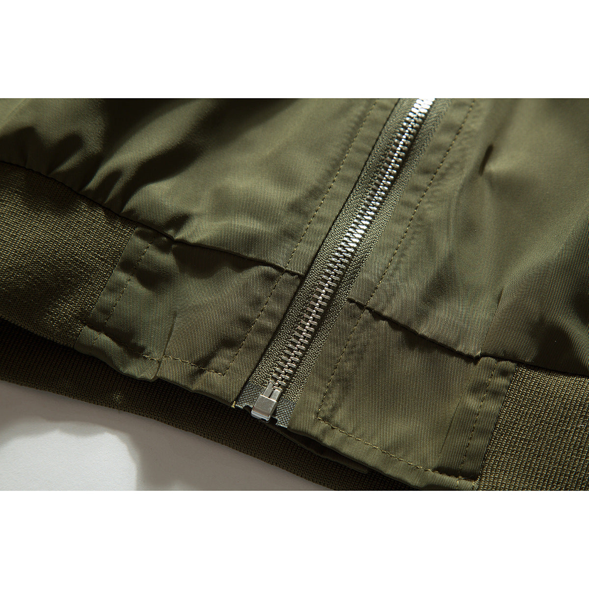 Close-up of the olive jacket's front zipper, stitched panels and ribbed hem.