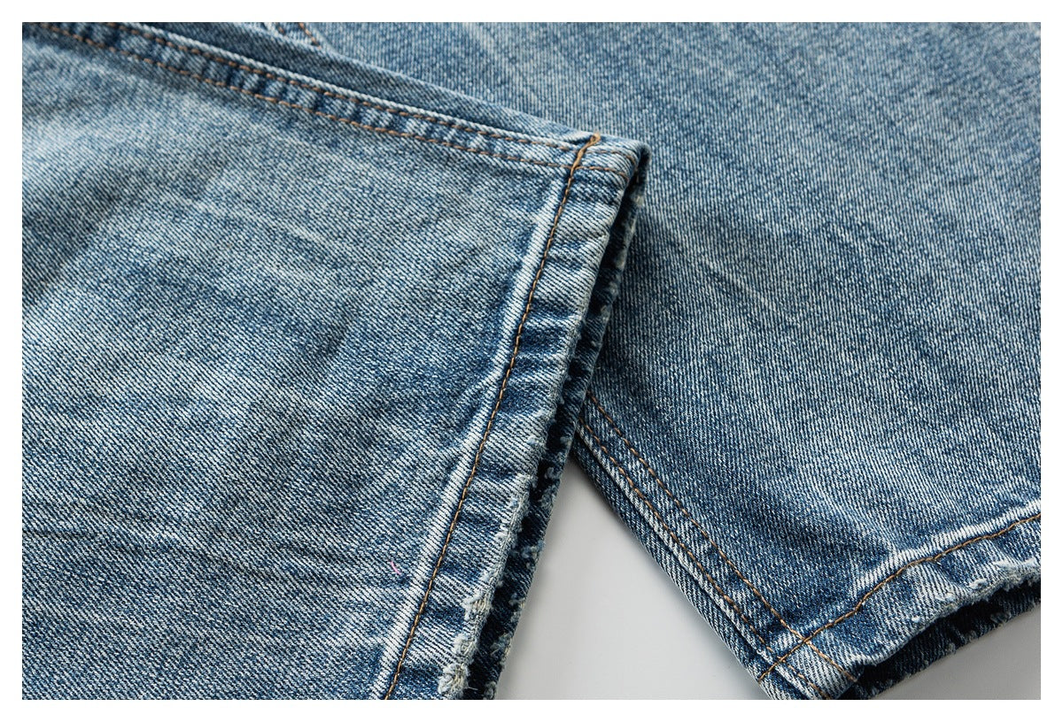 Close-up of faded blue denim hems with orange-brown stitching and a slightly frayed edge.