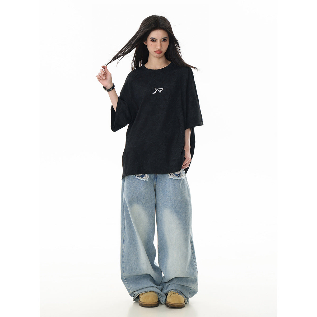 Model wearing an oversized black T-shirt with a small white chest emblem and light blue wide-leg jeans, front view.