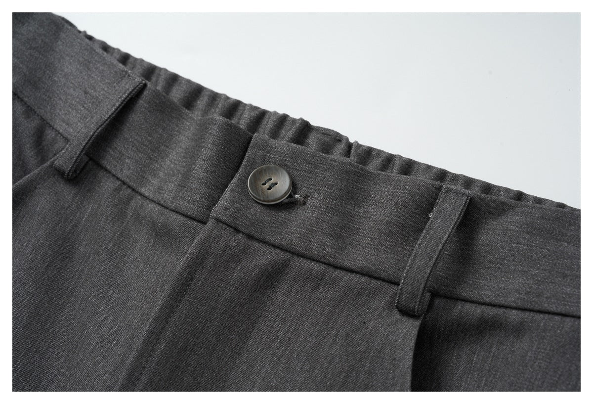 Close-up of charcoal trousers showing a buttoned waistband, belt loops, and front pleats.