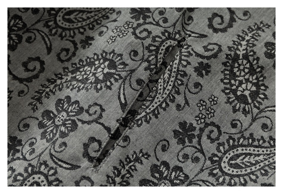 Close-up of a seam in gray fabric patterned with black flowers, paisley motifs, and curling vines.
