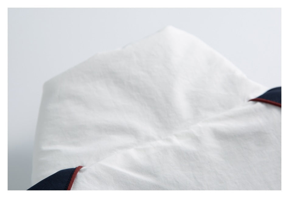 Close-up of white garment fabric with dark navy sections and narrow red piping at the edges.