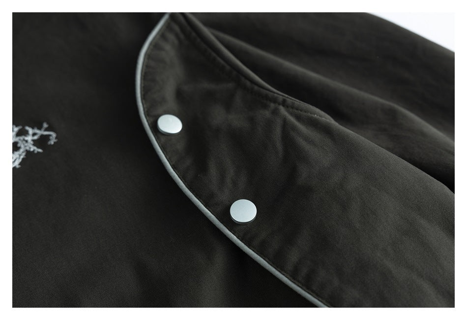 Close-up of black garment fabric with gray piping, two silver snaps, and part of an embroidered motif.