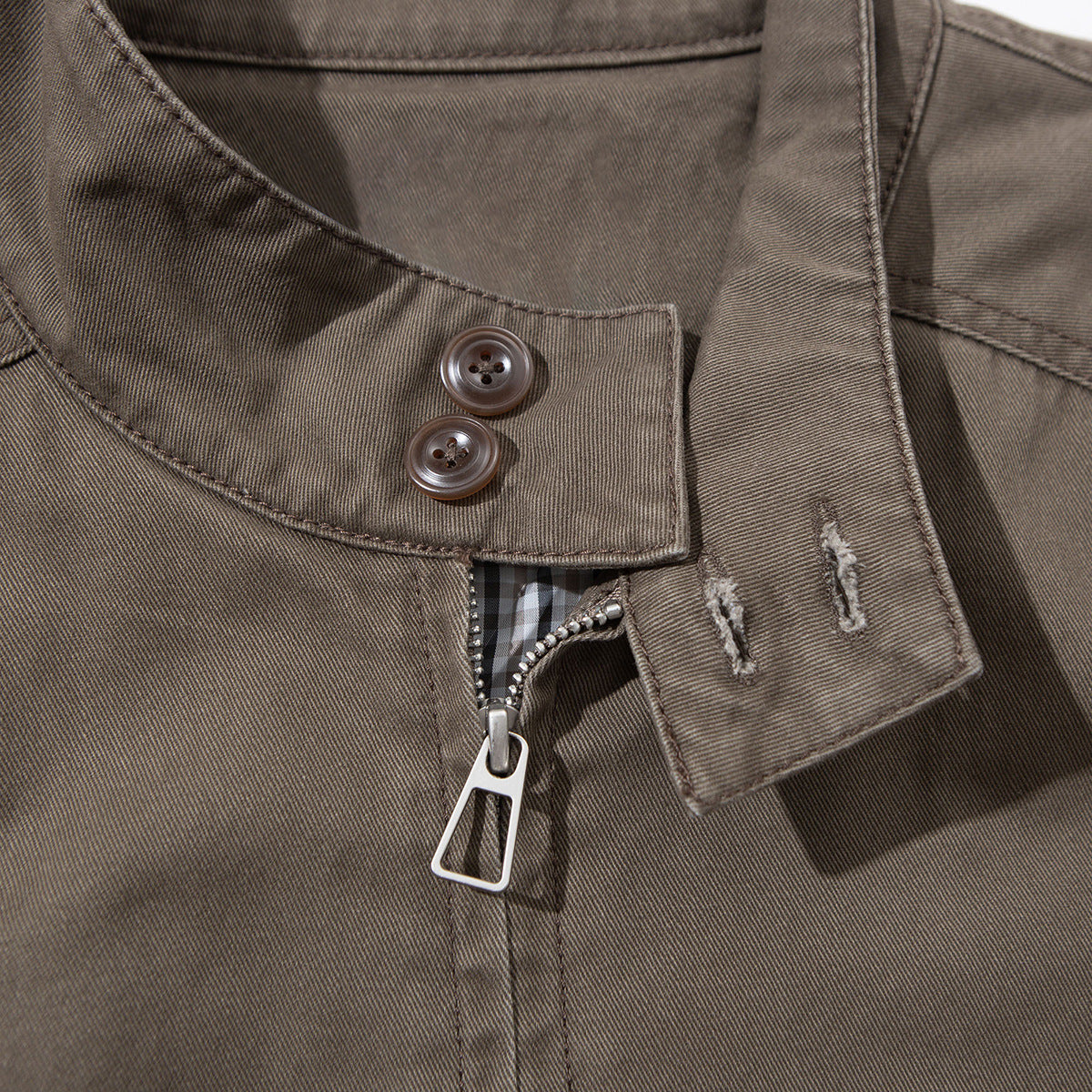 Close-up of a brown-gray jacket front with a buttoned zipper flap, metal zipper pull, and checked lining.
