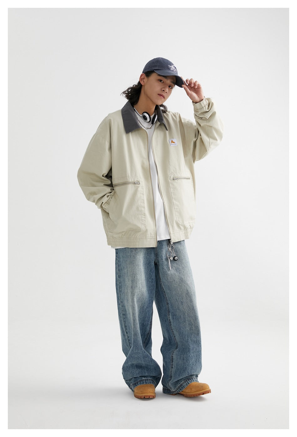 Model wearing a pale beige zip-front jacket with a gray collar and zip pockets, paired with loose blue jeans.