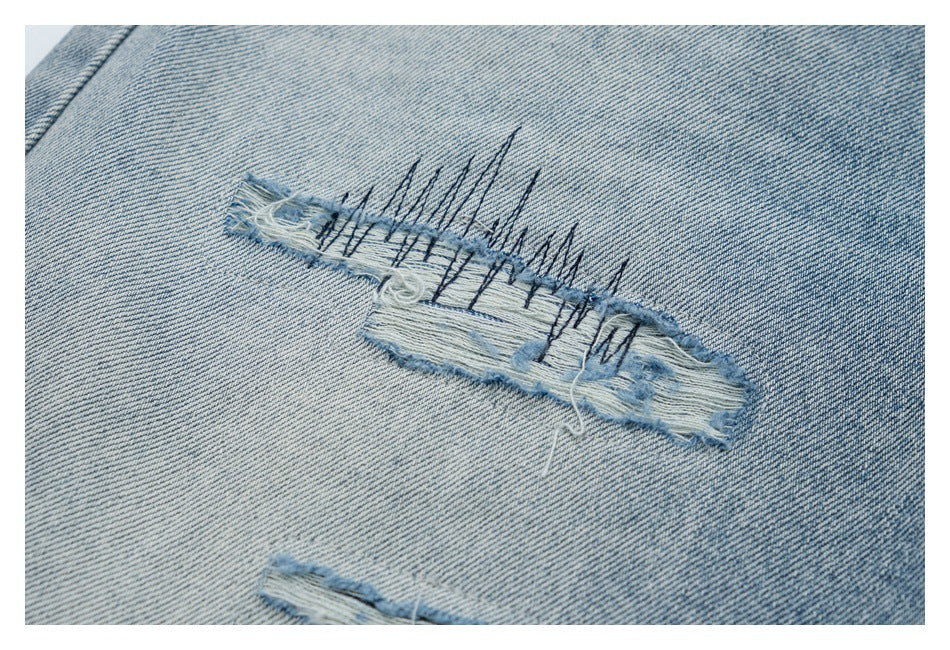 Close-up of a frayed horizontal tear with dark stitching on light blue denim.