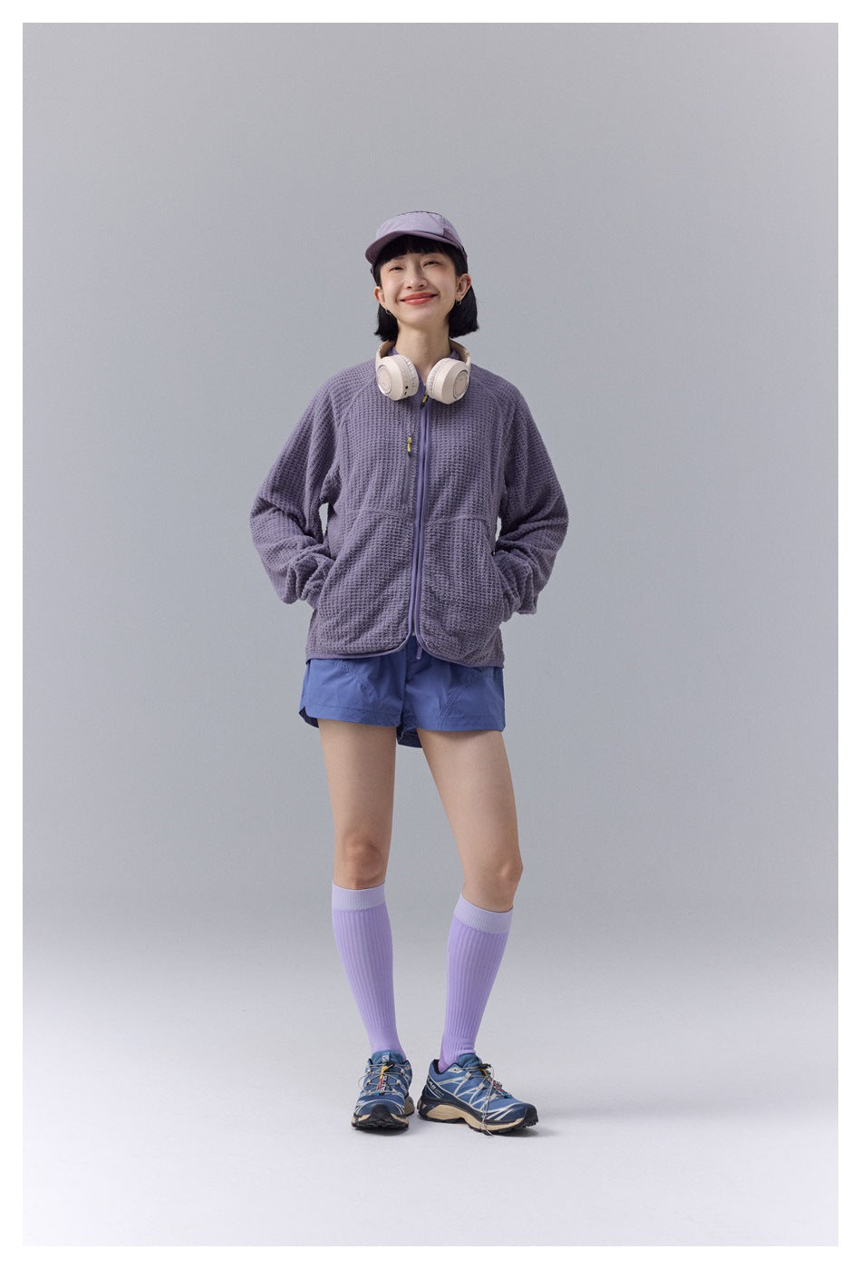 Model wearing a textured lavender zip jacket, blue shorts, and lavender cap, shown from the front.