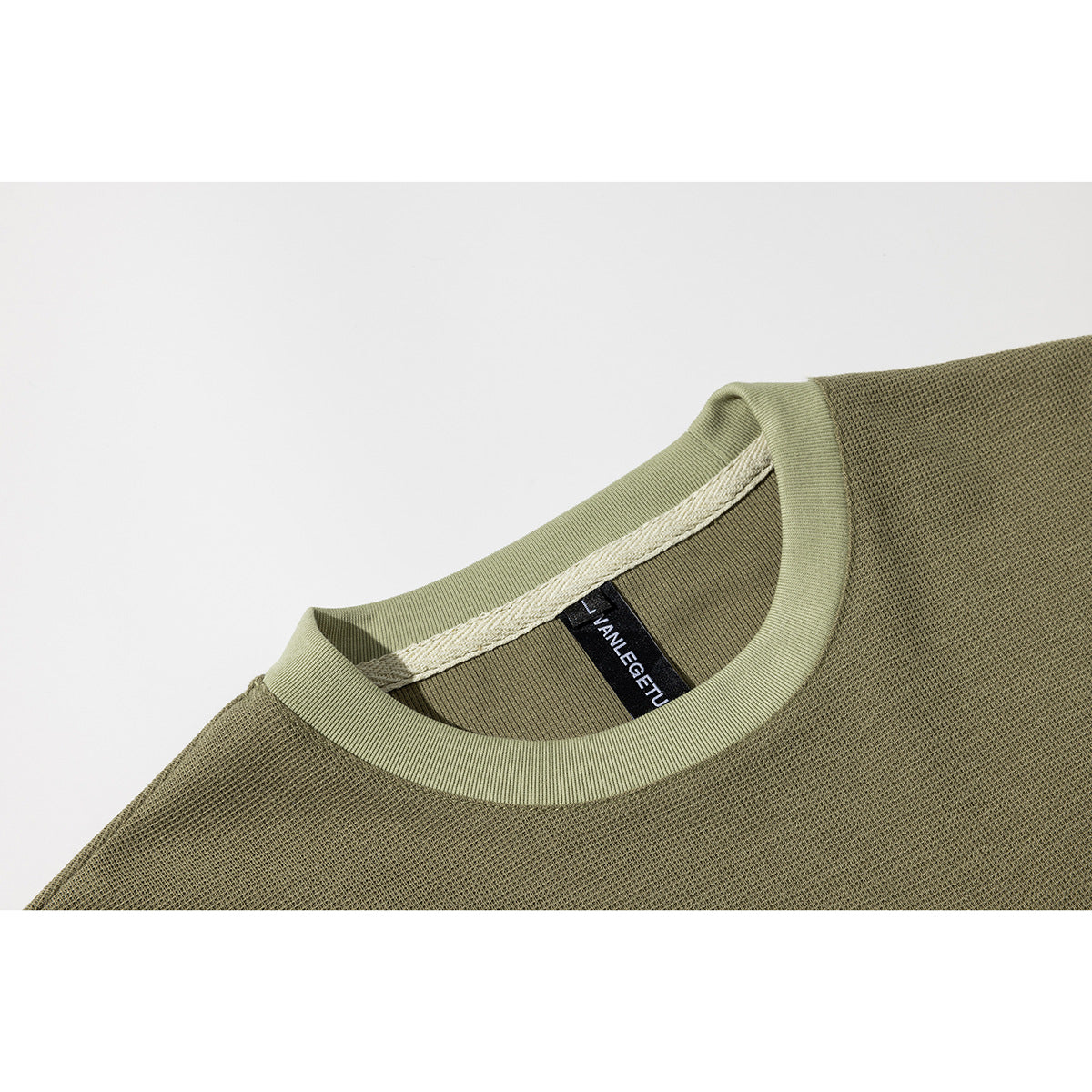 Close-up of an olive T-shirt's ribbed crew neck, pale inner seam tape, and black neck label.