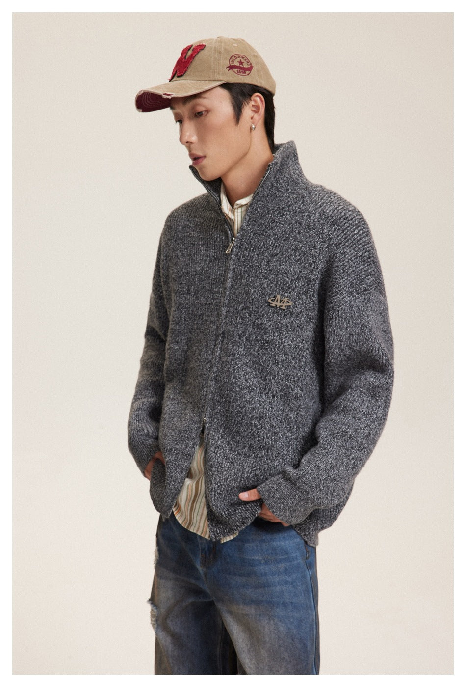 Three-quarter view of a model wearing a charcoal textured zip-up cardigan with raised collar and blue jeans.