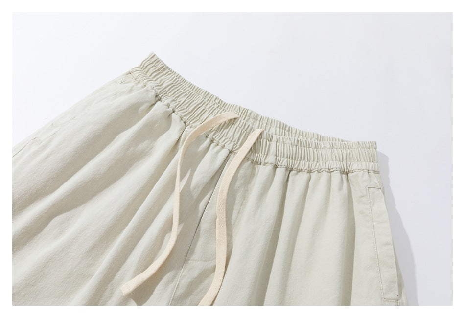 Close-up of light beige trousers with an elastic waistband, long drawstring and side pocket.