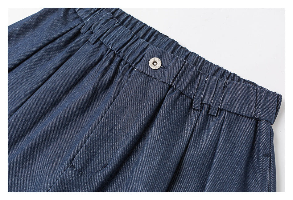 Close-up of navy trousers showing the gathered elastic waistband, belt loops, metal button, and front pleats.