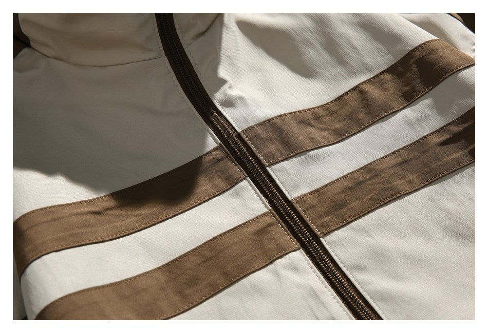 Close-up of a beige jacket with brown horizontal panels and a dark brown front zipper.