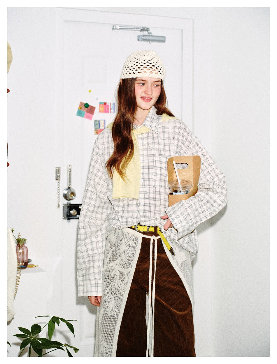 Model wearing a light plaid button-up shirt with brown pants, a white lace apron and a crochet cap.