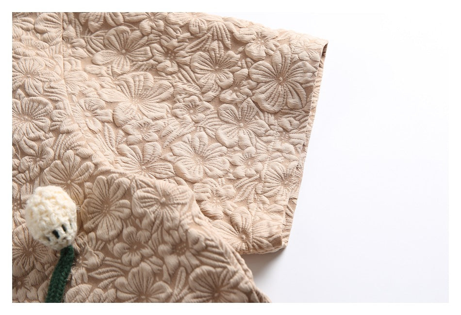 Close-up of the beige floral shirt sleeve and textured fabric, with a small crocheted flower accent.