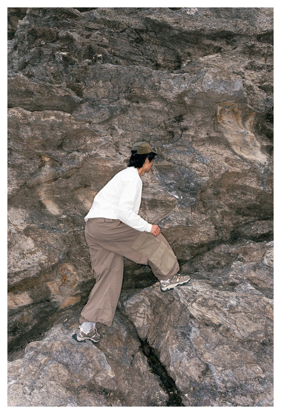 Side and rear view of a model climbing rocks in a white long-sleeve top and taupe cargo pants.