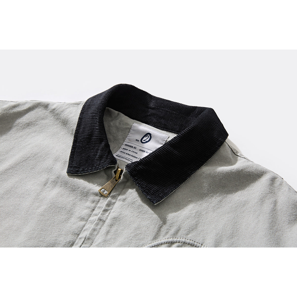 Close-up of a light gray jacket's black ribbed collar, brass zipper pull, and sewn neck label.