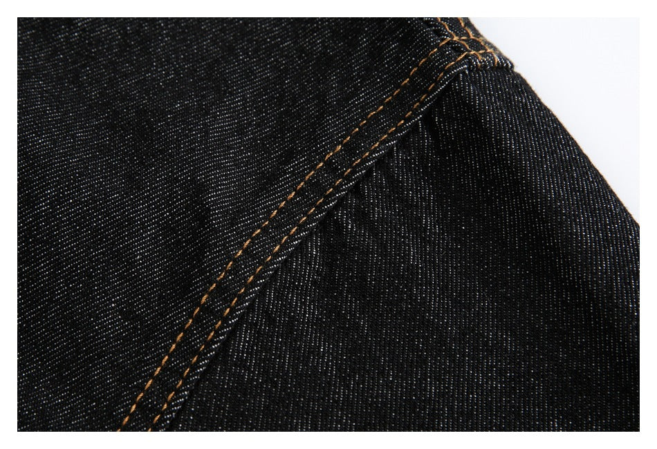 Close-up of black denim fabric and a curved seam with contrasting orange stitching.