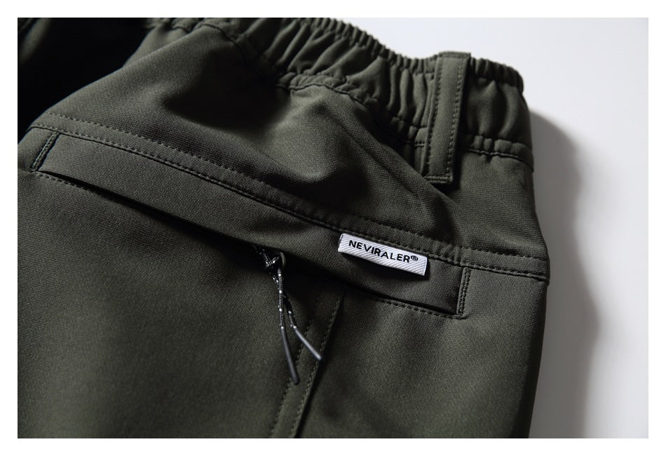Close-up of the back waistband and pocket of dark olive pants, with a small brand label.