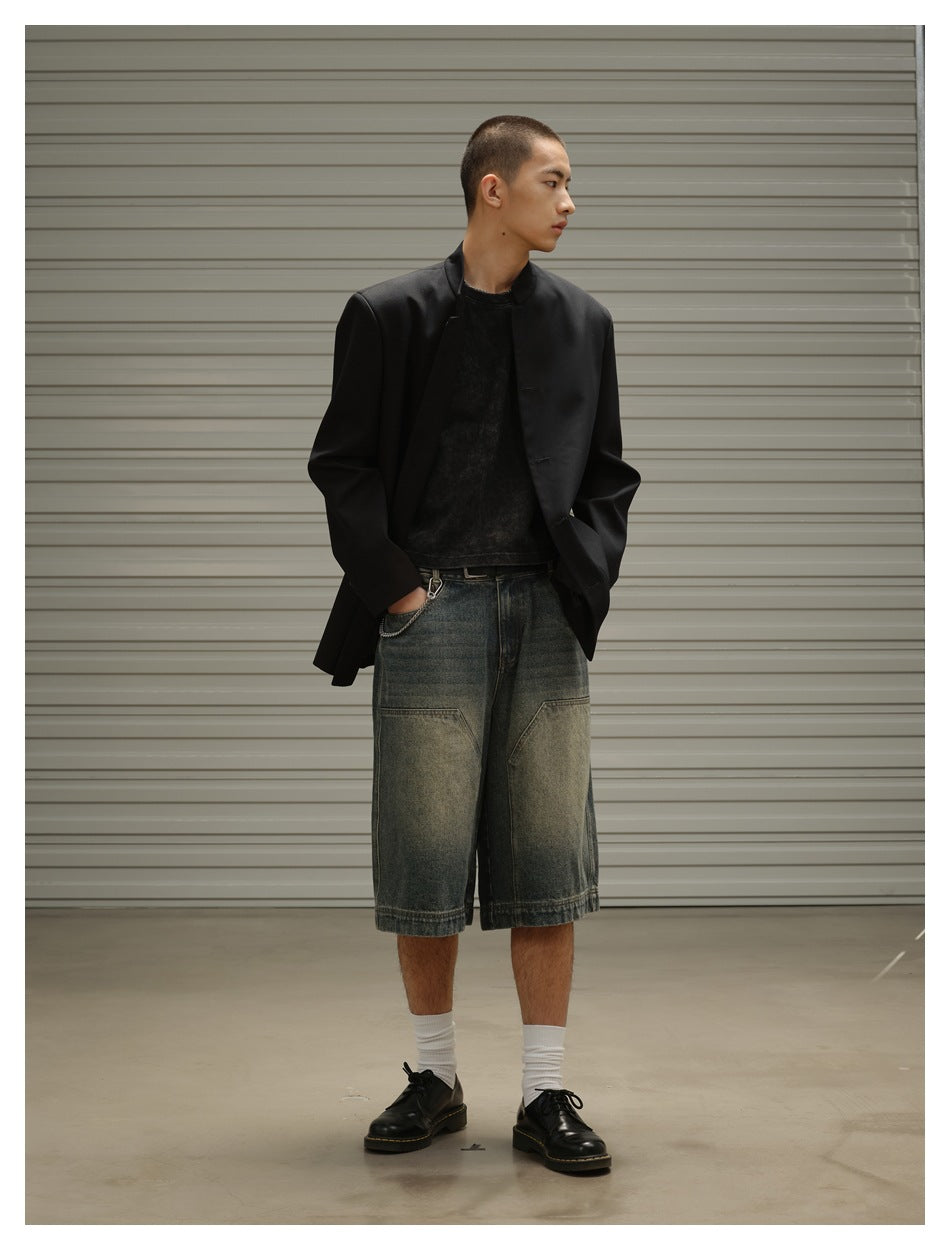 Model wearing an open black stand-collar jacket with faded denim shorts, a dark T-shirt, white socks and black shoes.