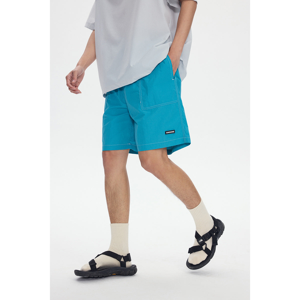 Cropped view of a model wearing bright turquoise shorts with a large patch pocket and white topstitching.