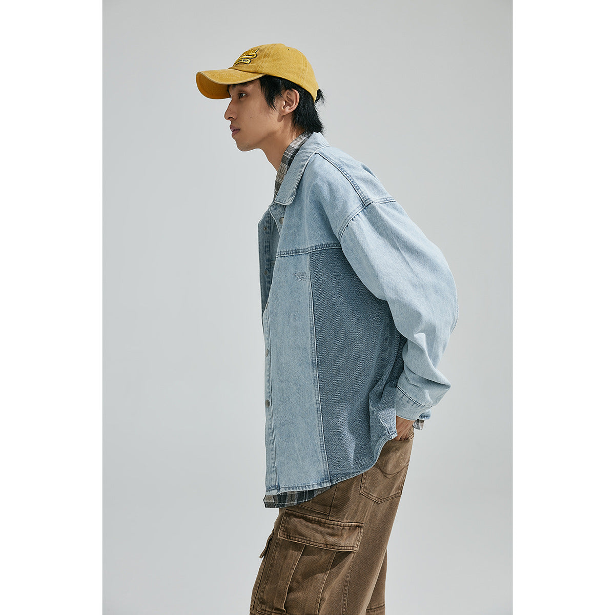 Side view of a model wearing a light-blue denim jacket with a darker contrast side panel and brown cargo pants.