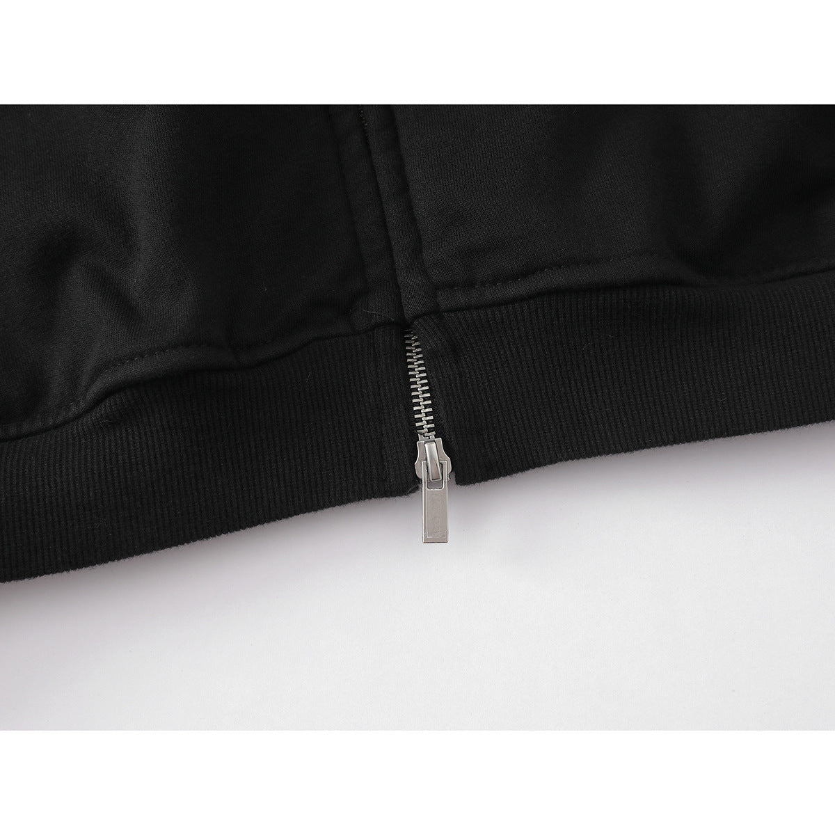 Close-up of the black hoodie’s ribbed hem and silver zipper pull.