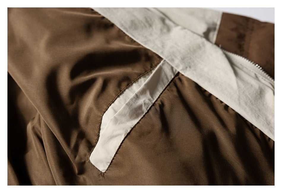 Close-up of a brown garment with cream contrast panels, visible stitching, and a metal zipper.