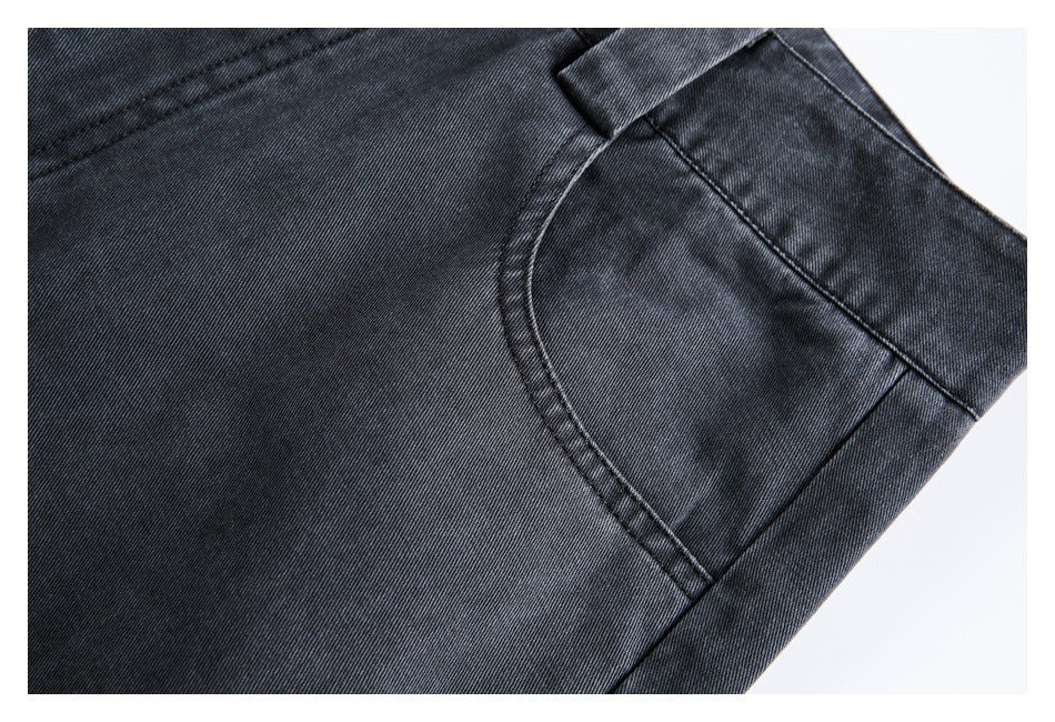 Close-up of dark charcoal denim texture, stitching and curved front pocket.
