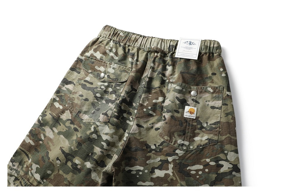 Cropped back view of green-brown camouflage trousers with an elastic waistband, two flap pockets, and attached tags.
