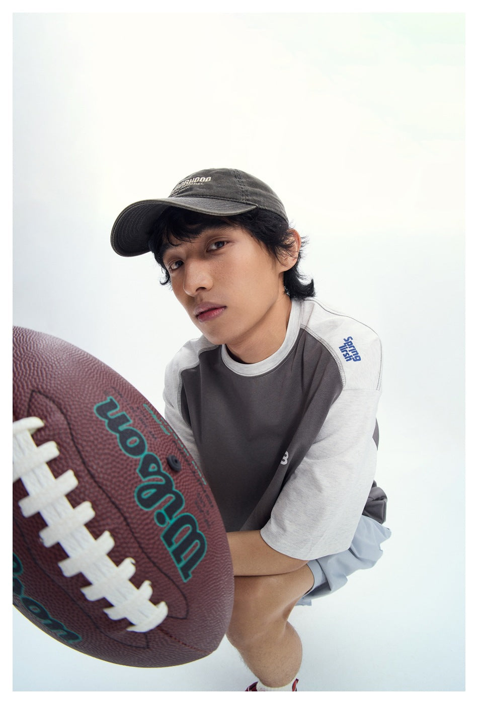 Person in a cap and gray raglan T-shirt with light gray sleeves, crouching with a football